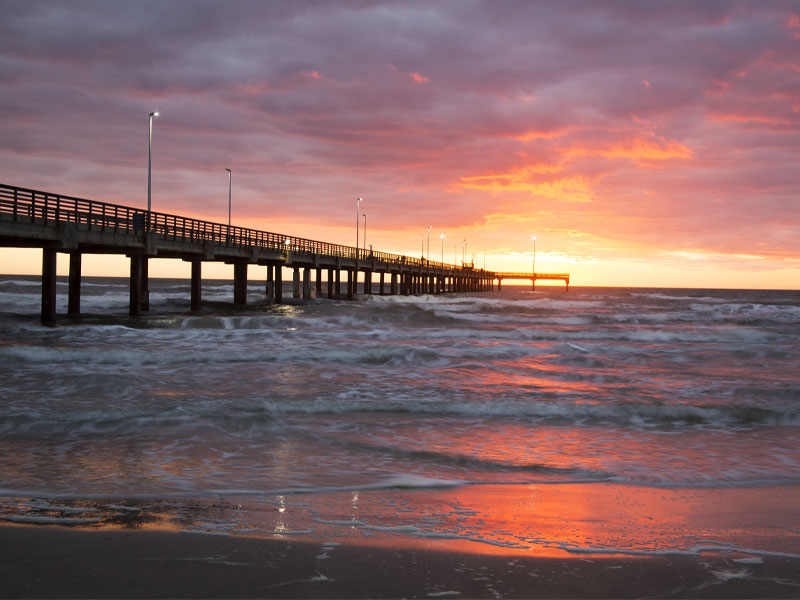 Pier extending into the ocean at sunset with waves along the shore